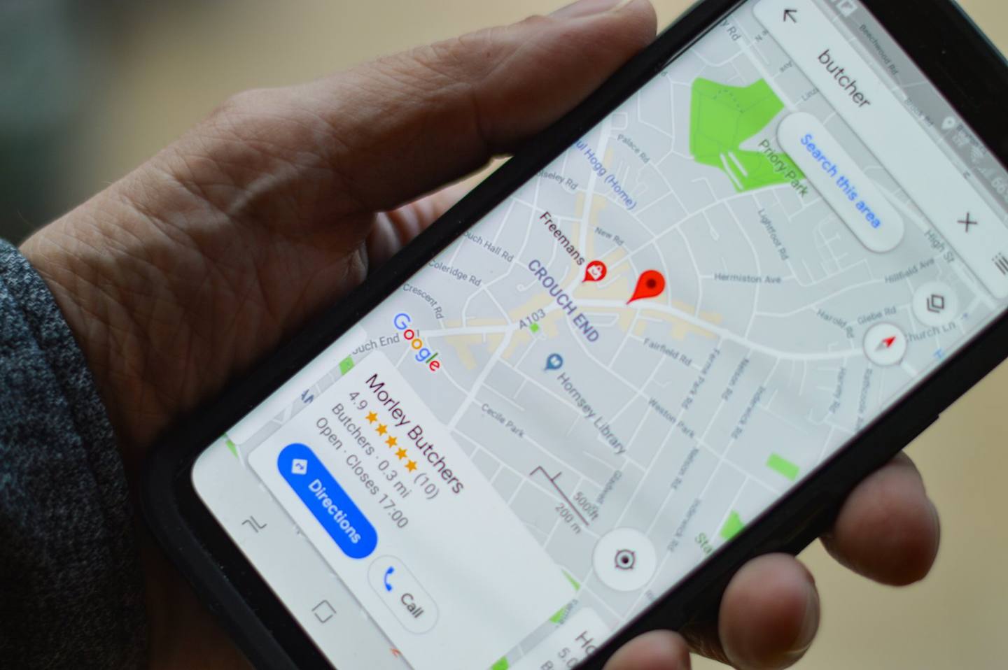 A hand holding a phone showing a local business on Google Maps