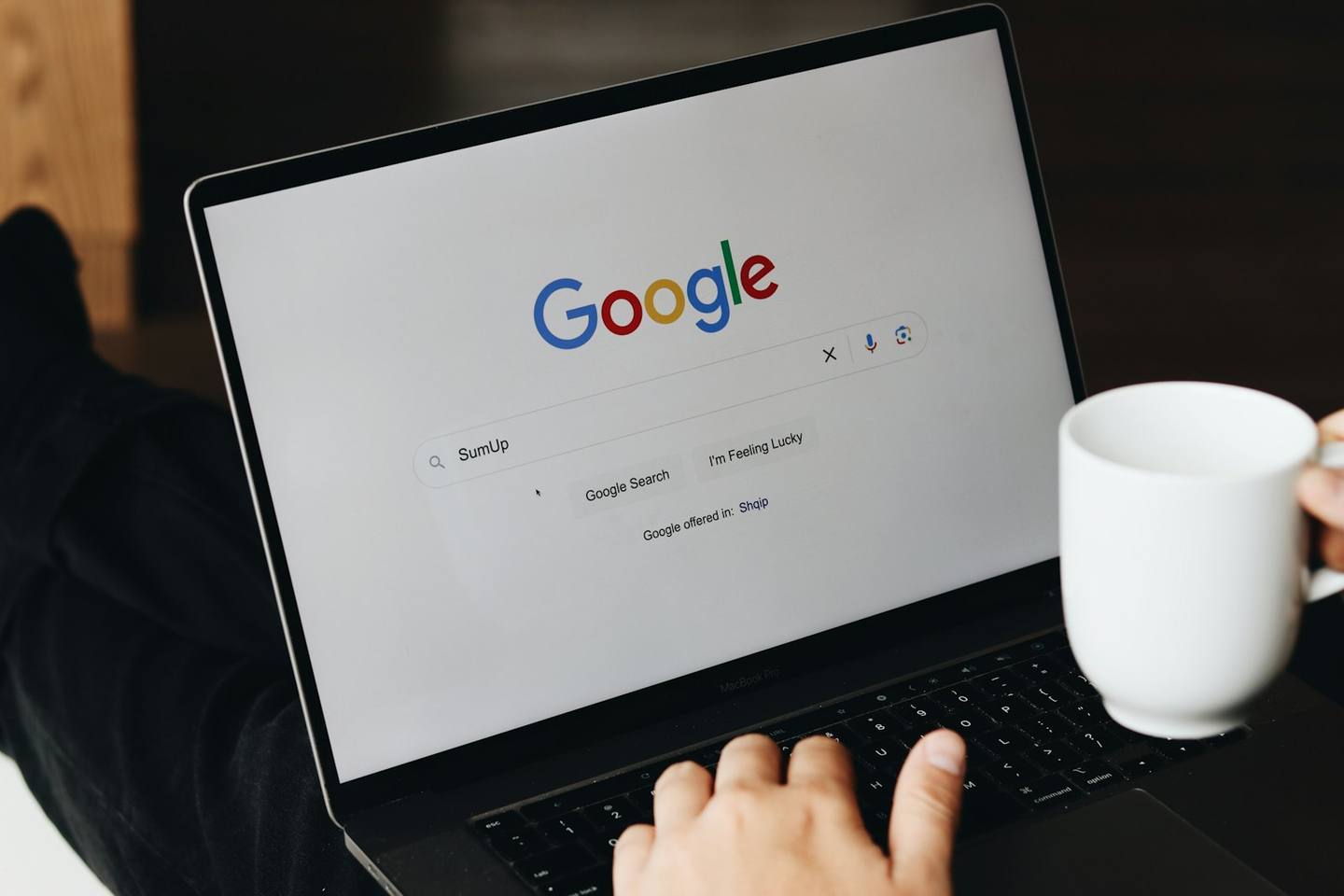A laptop open on the Google search page beside a coffee cup