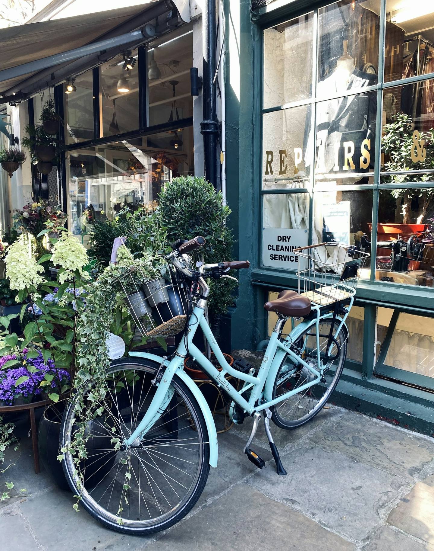 A pale blue bicycle full of flowers outside a green shopfront