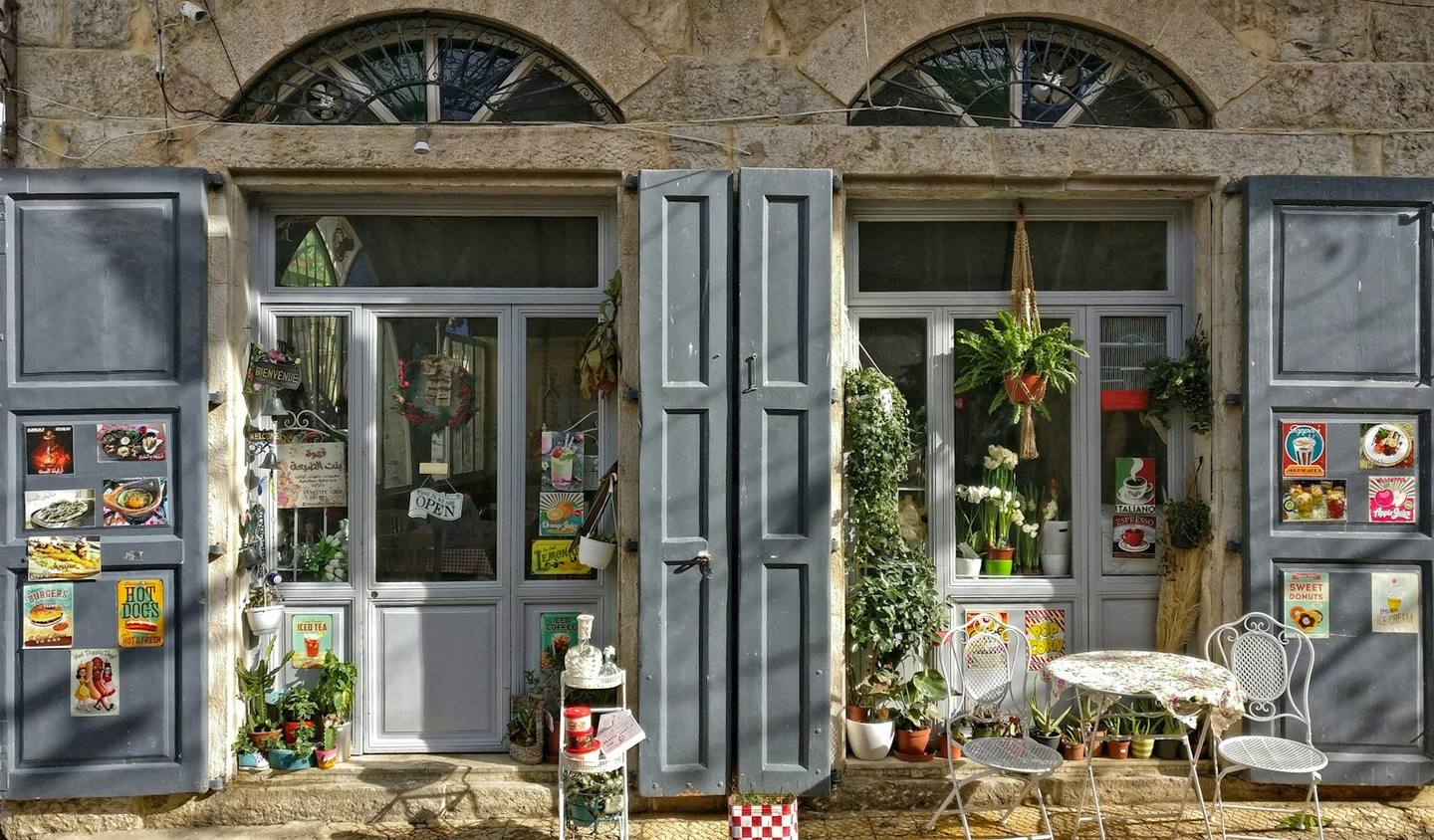 A stone shopfront with grey shutters and bistro chairs
