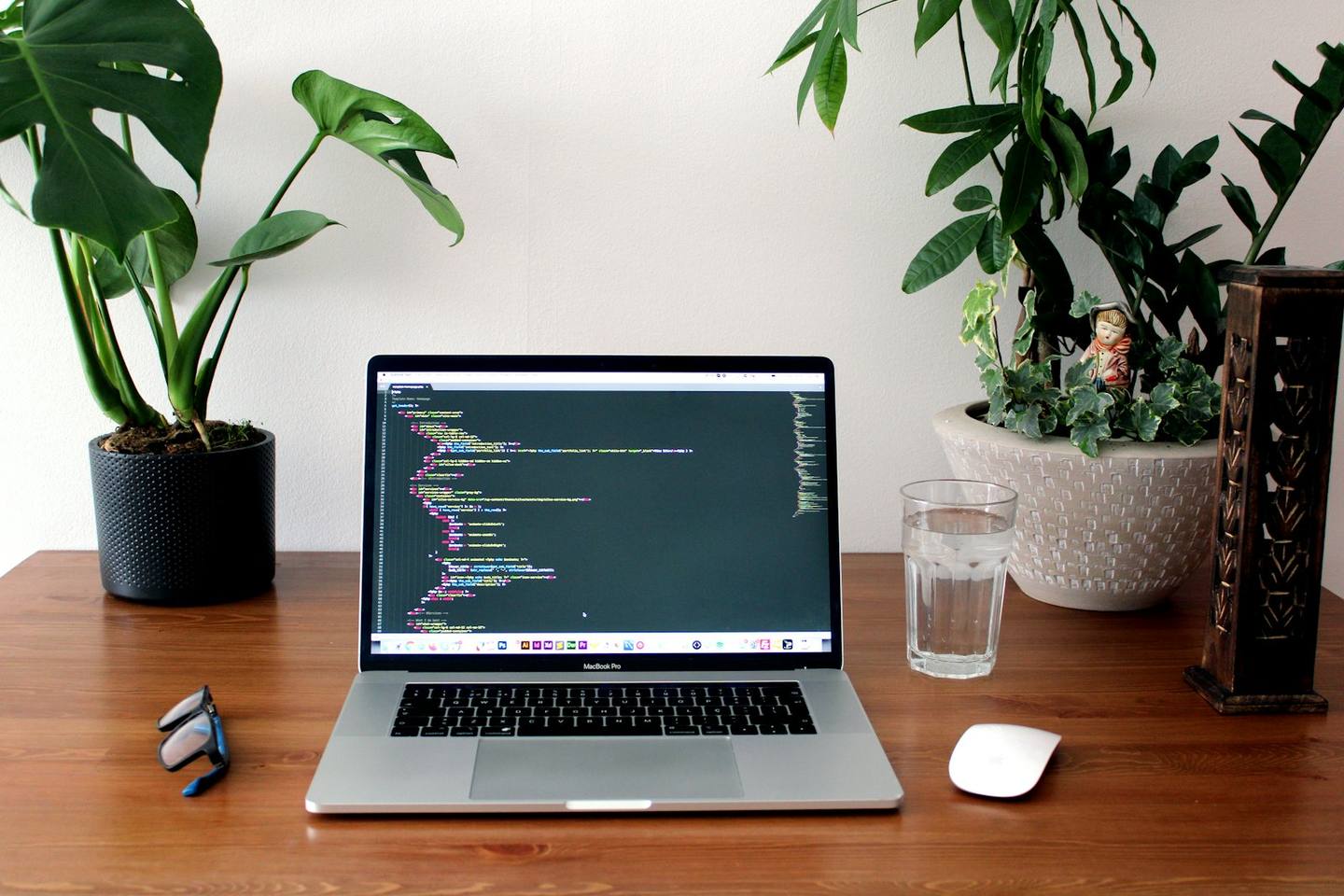 A laptop showing code on a wooden desk surrounded by plants